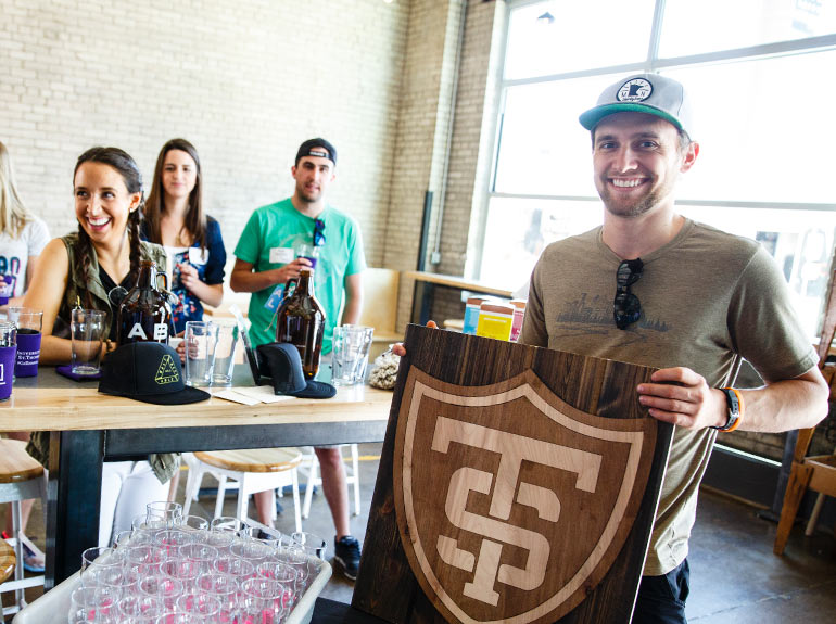 Alum Garrett Faust, '13, owner of Uptown Woodworks, holds a St. Thomas shield sign made by his business during a Young Alumni Council social event.