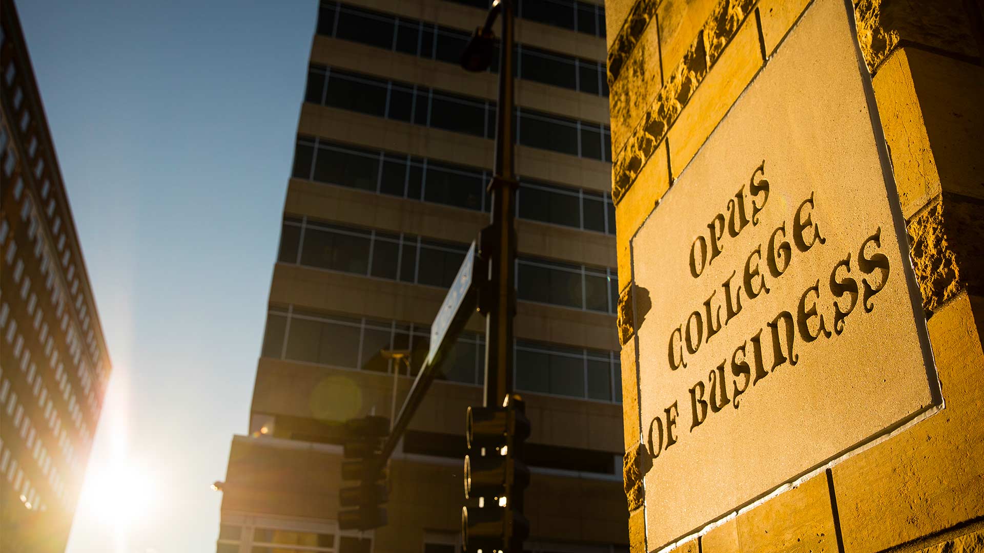 The sun shines on a sign for Opus College of Business.