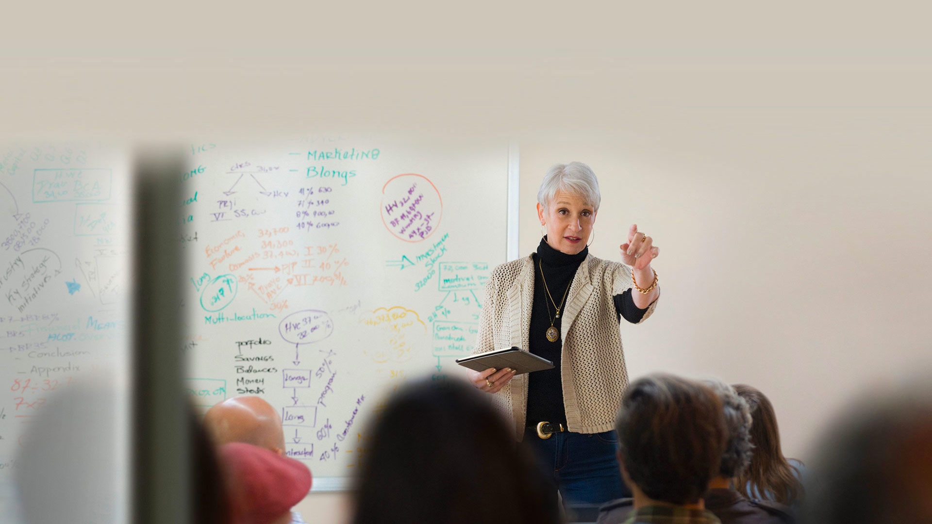 Professor lecturing in front of a whiteboard full of notes points to a student.