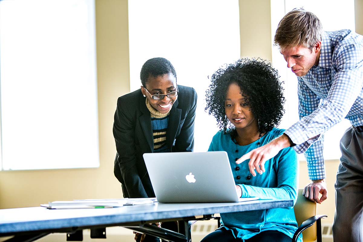 Three MBA students work around a computer in Schulze Hall in Minneapolis, two stand and look over the shoulder of the third student.