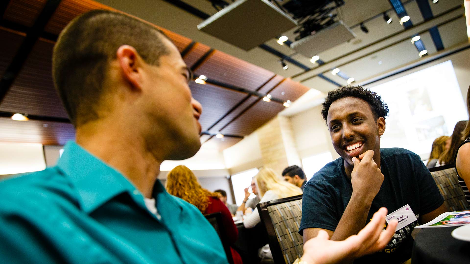Two students smiling and holding a conversation in a get together.