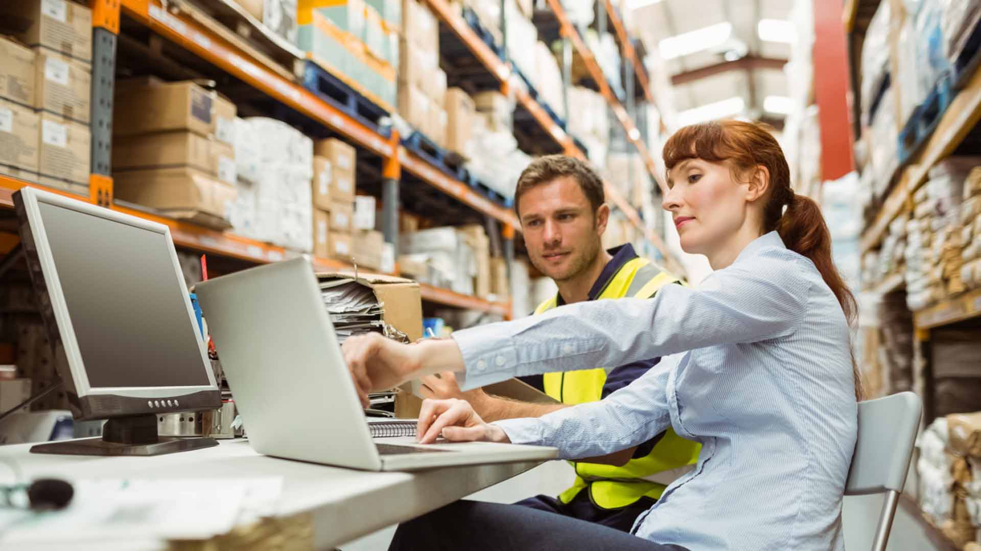 Two people view a computer in a warehouse