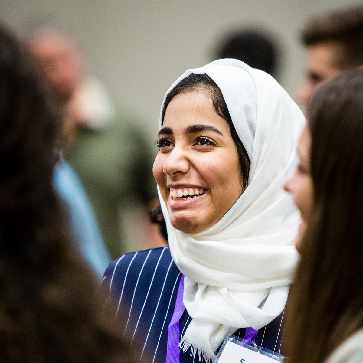 Student smiles brightly while mingling with other students and alumni.