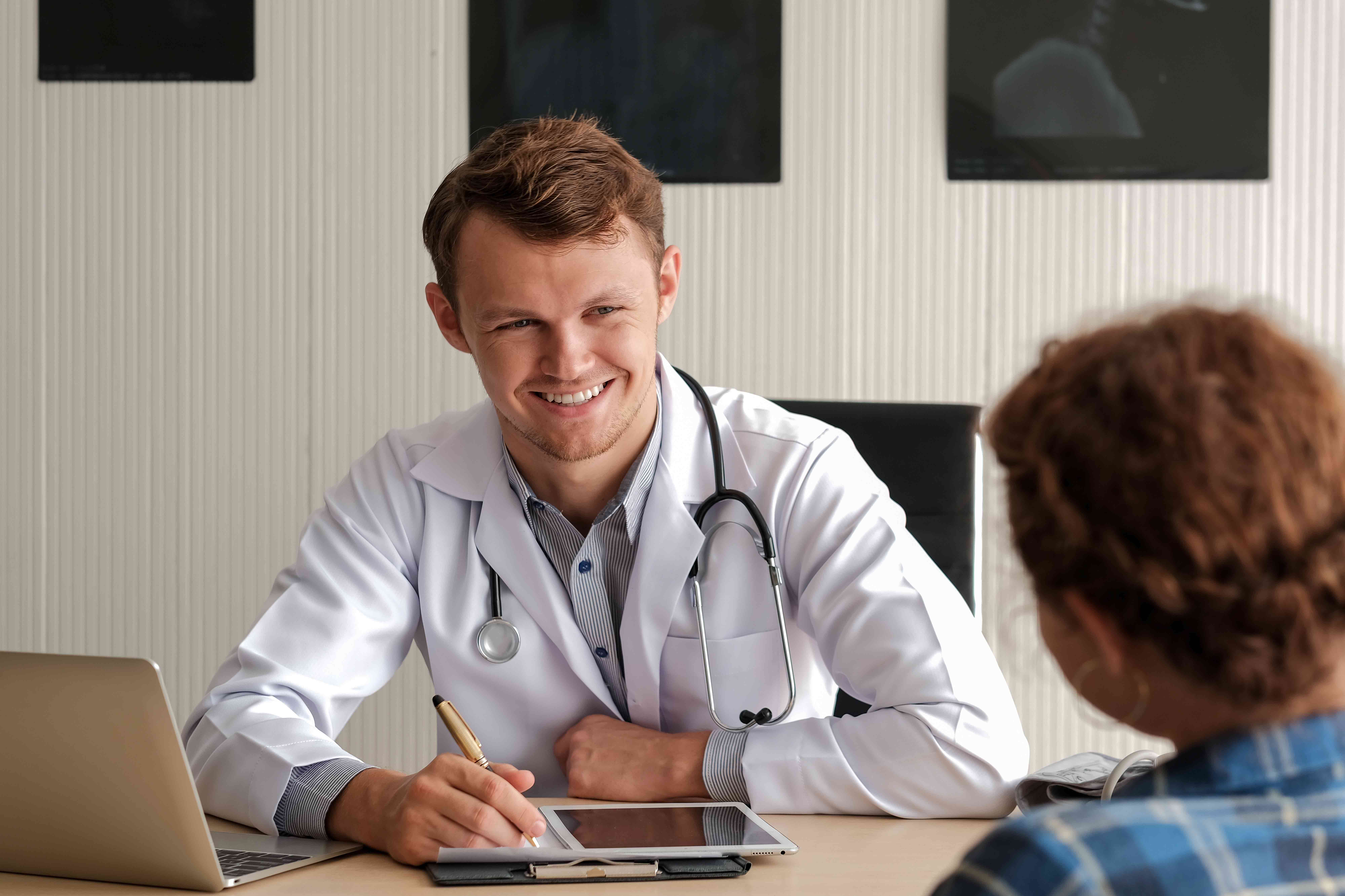 A doctor smiling and sitting across a table from, possibly, a patient. 