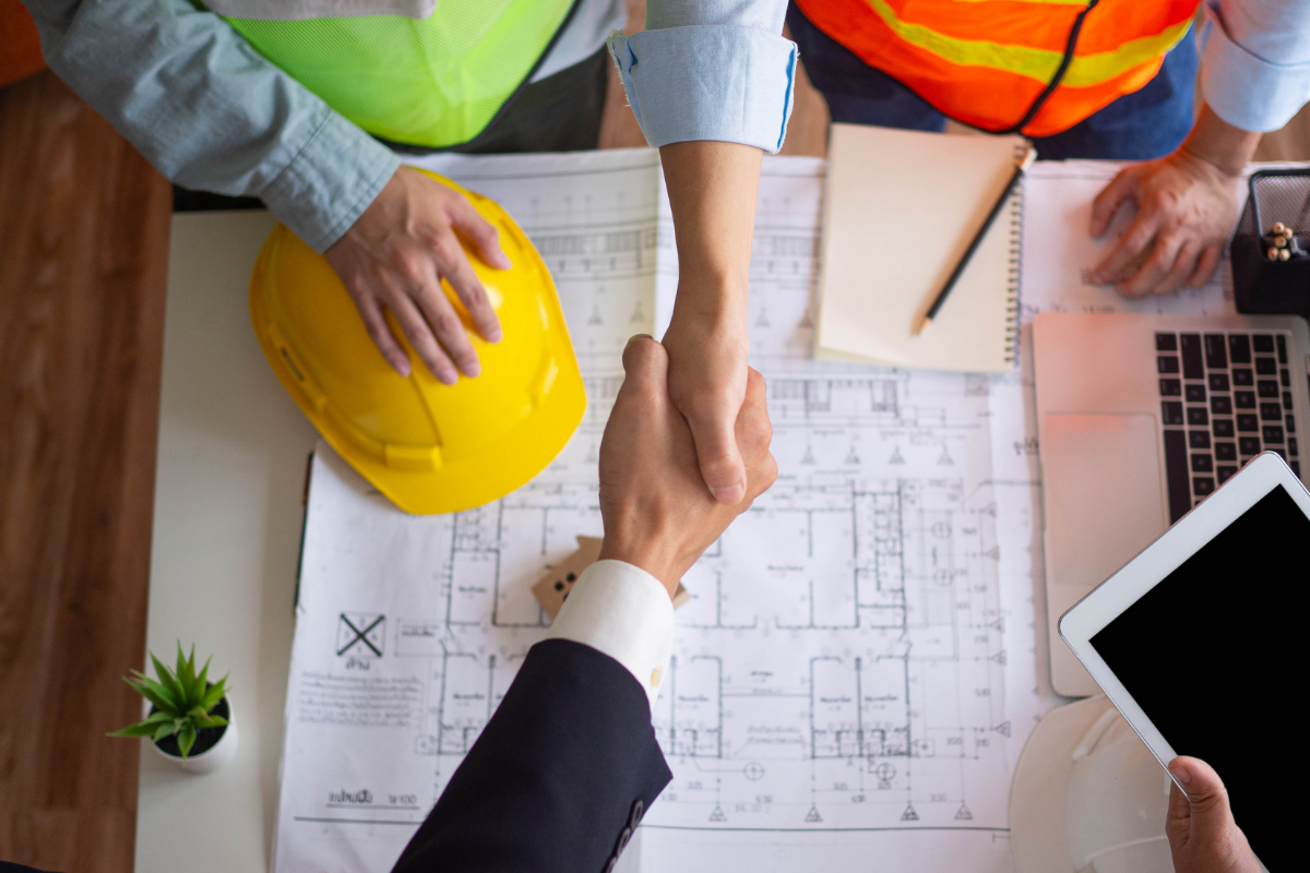 Construction workers shake hands over building plans.