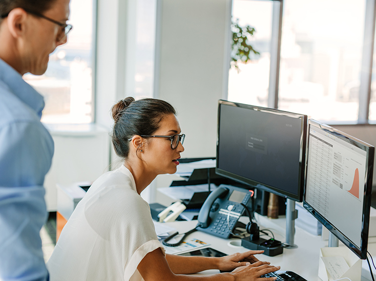 Two professionals studying a computer screen with a graph and charts on it.