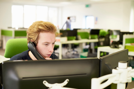 Business man sitting in front of a computer and speaking on phone.