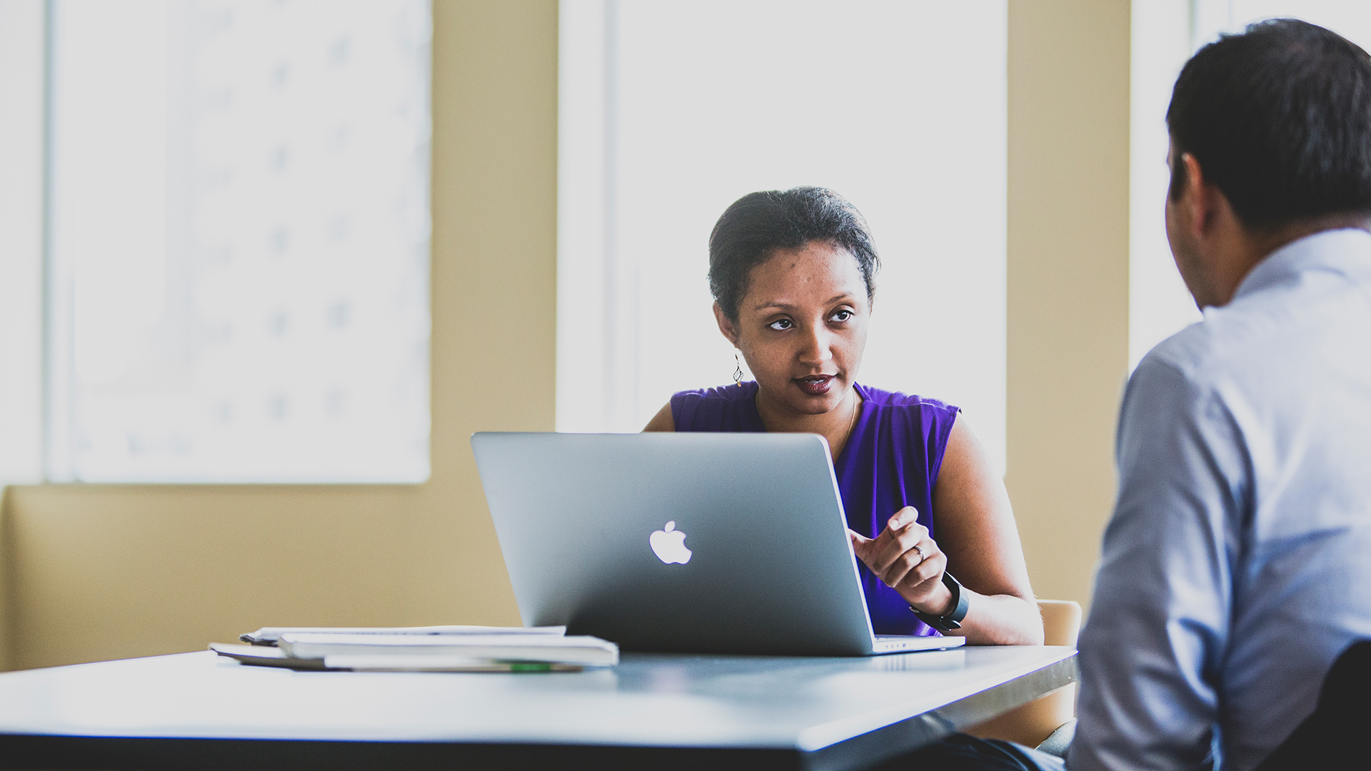 Business student sitting in front of a laptop computer having a discussion with another student.