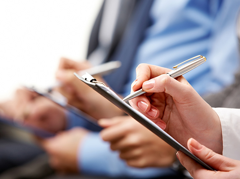 A person writing on a clipboard with a shiny pen.