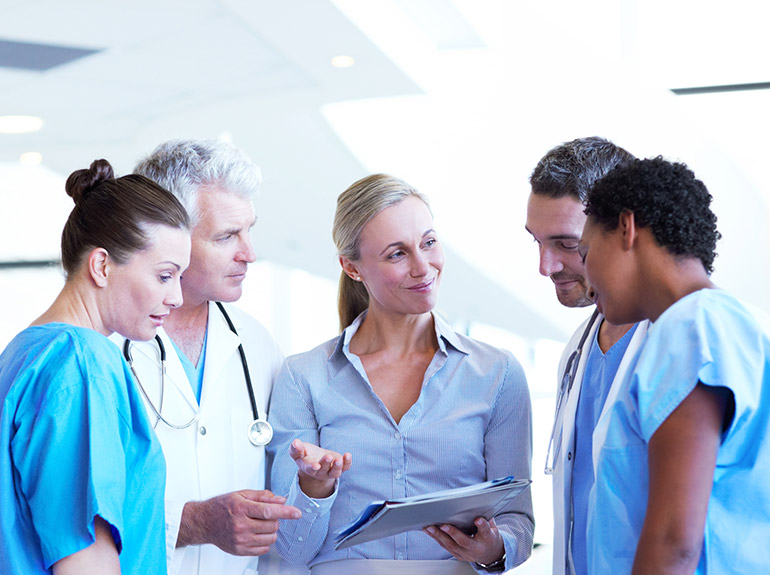 A group of five doctors engaging in discussion regarding results revealed on the clipboard.