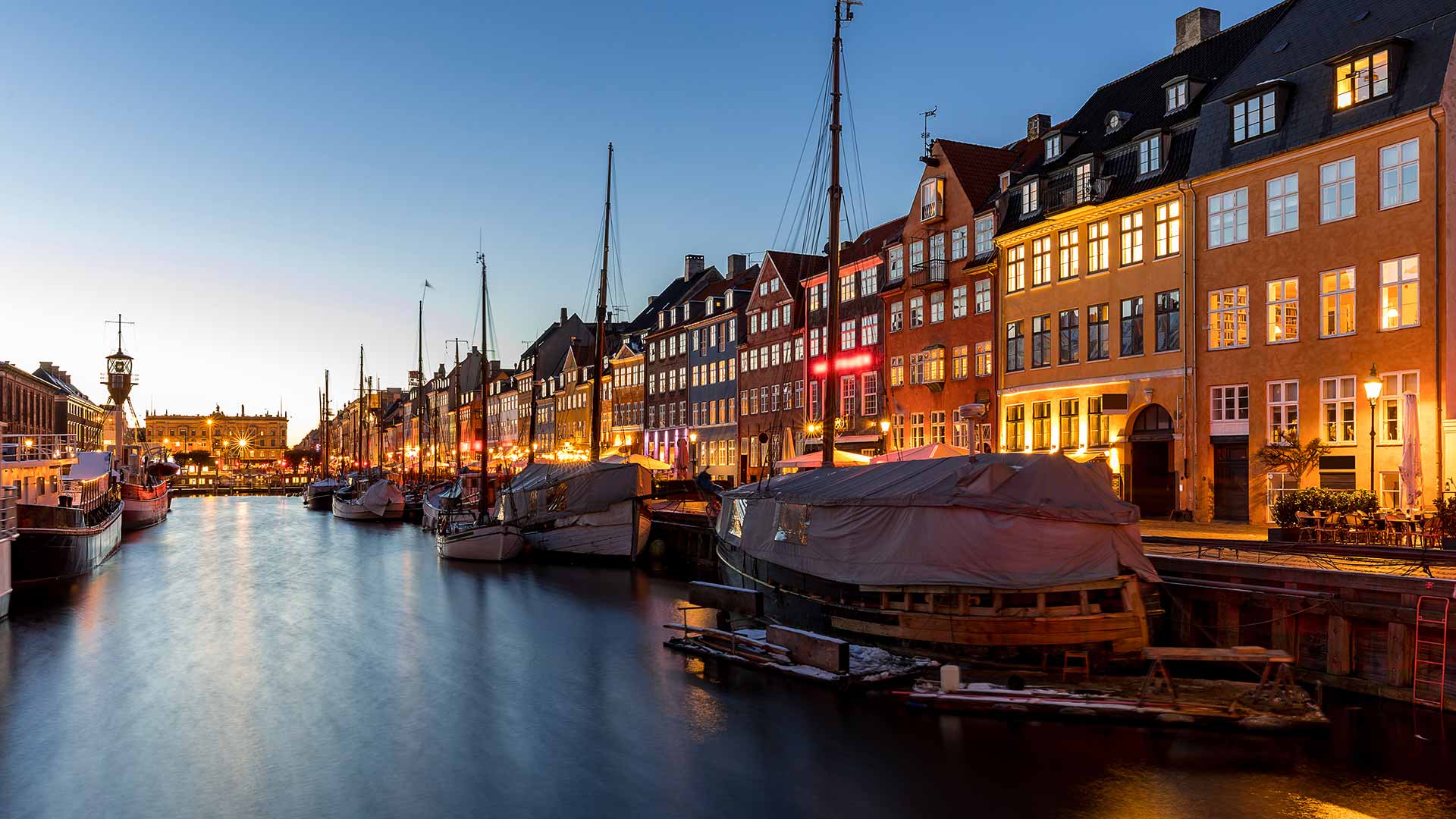 Sailboats stored on a building lined canal in an international city at sunset.