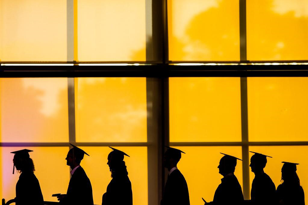 Students walking in cap and gown at a commencement ceremony.