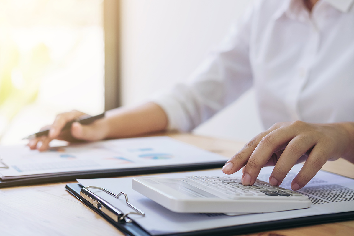 Professional calculating and analyzing financial graph data with calculator and laptop.