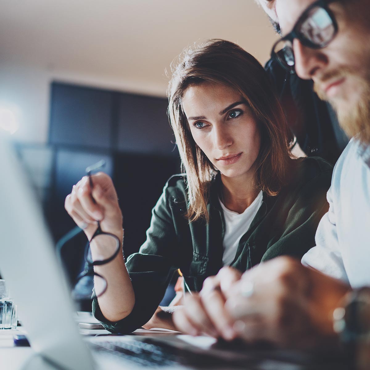 Two professionals regard the laptop in front of them. 