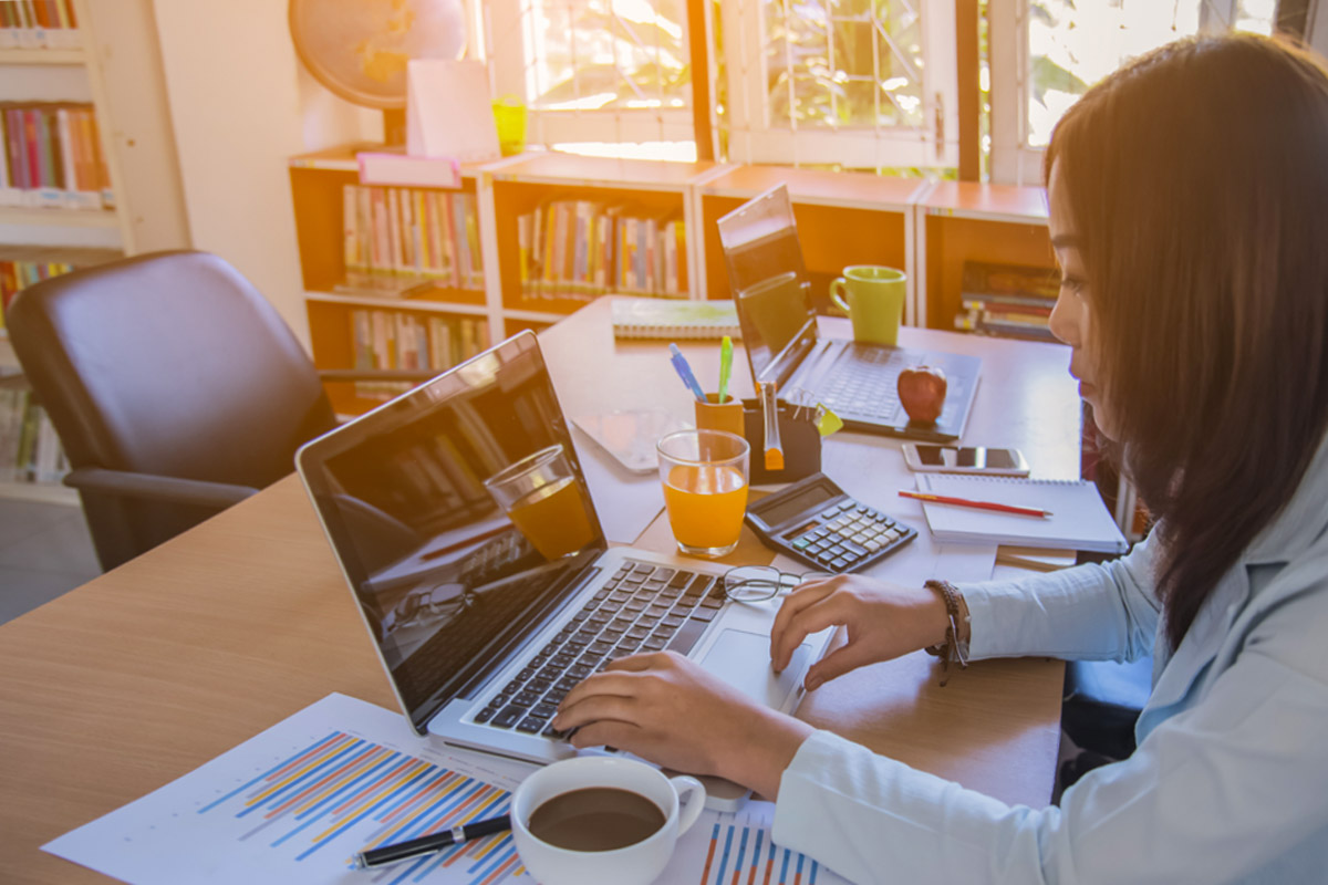 Woman working at office with laptop while drinking coffee.