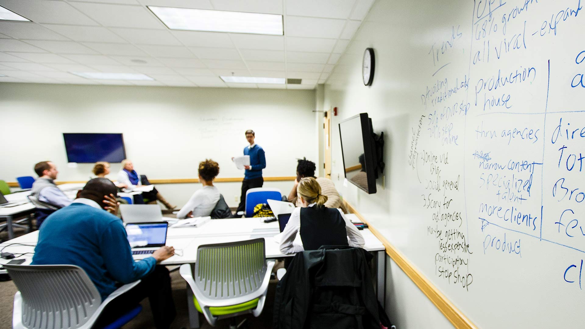 A group of students listen to their professor as he lectures. 
