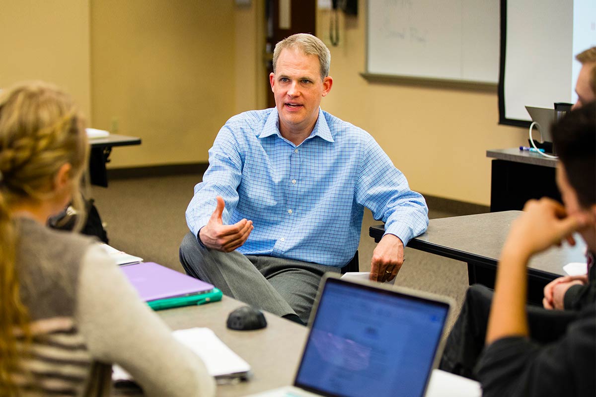 Professor lecturing students in small class room.