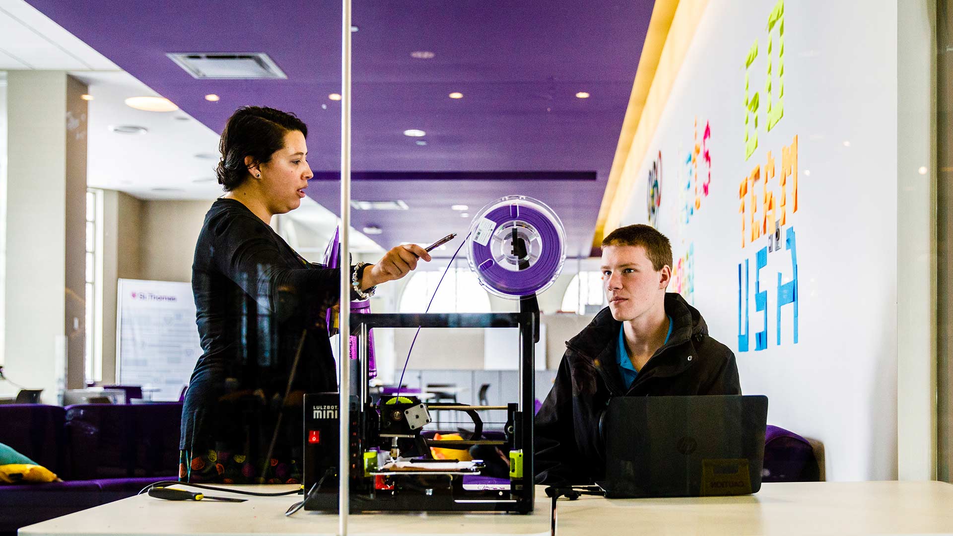 Two people work with a 3D printer in the create space.