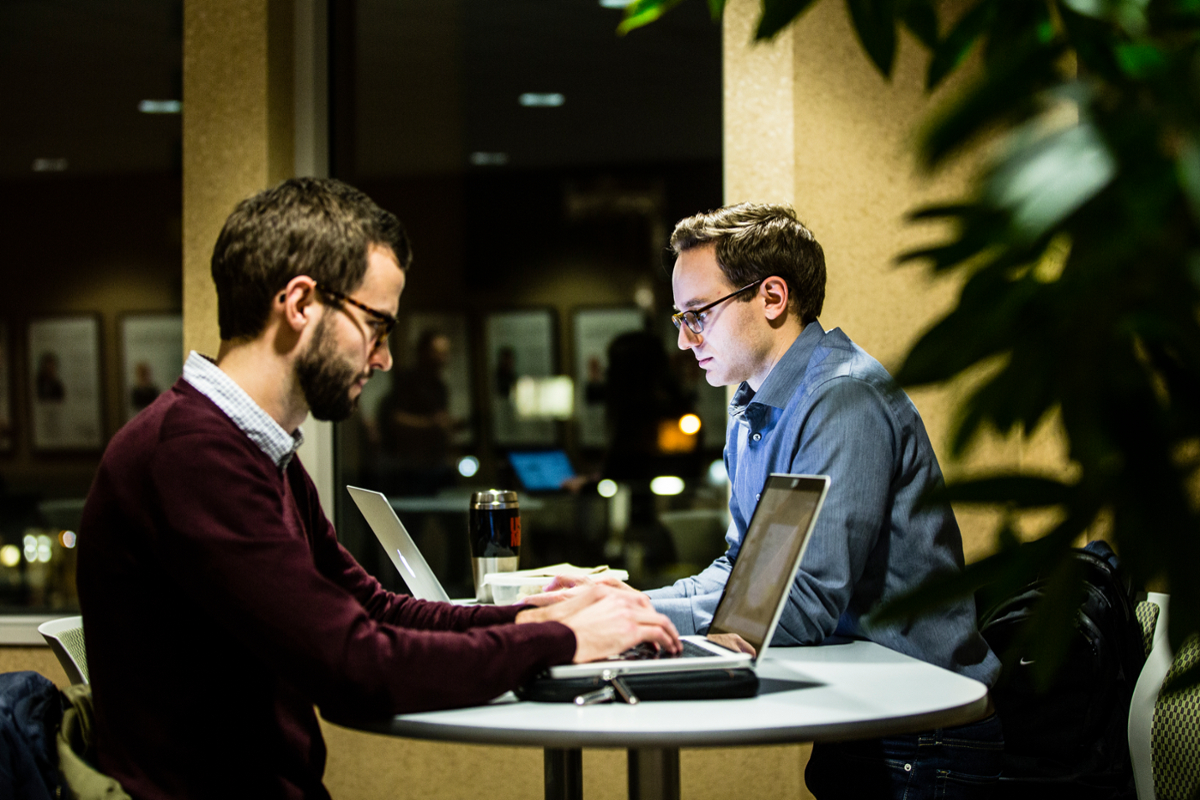Two students work on laptops at a tall table