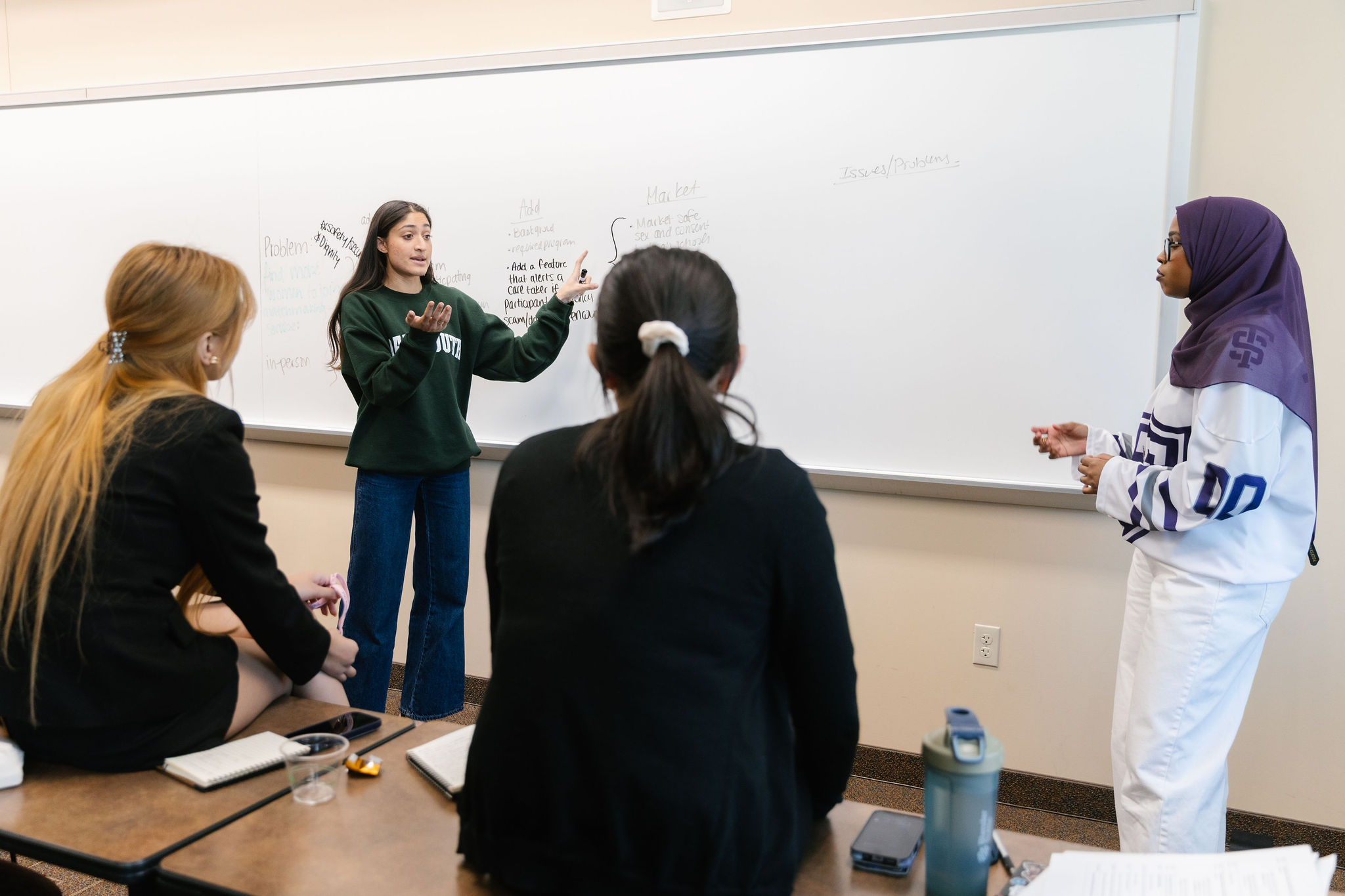 Students from different teams collaborate on projects at a table.