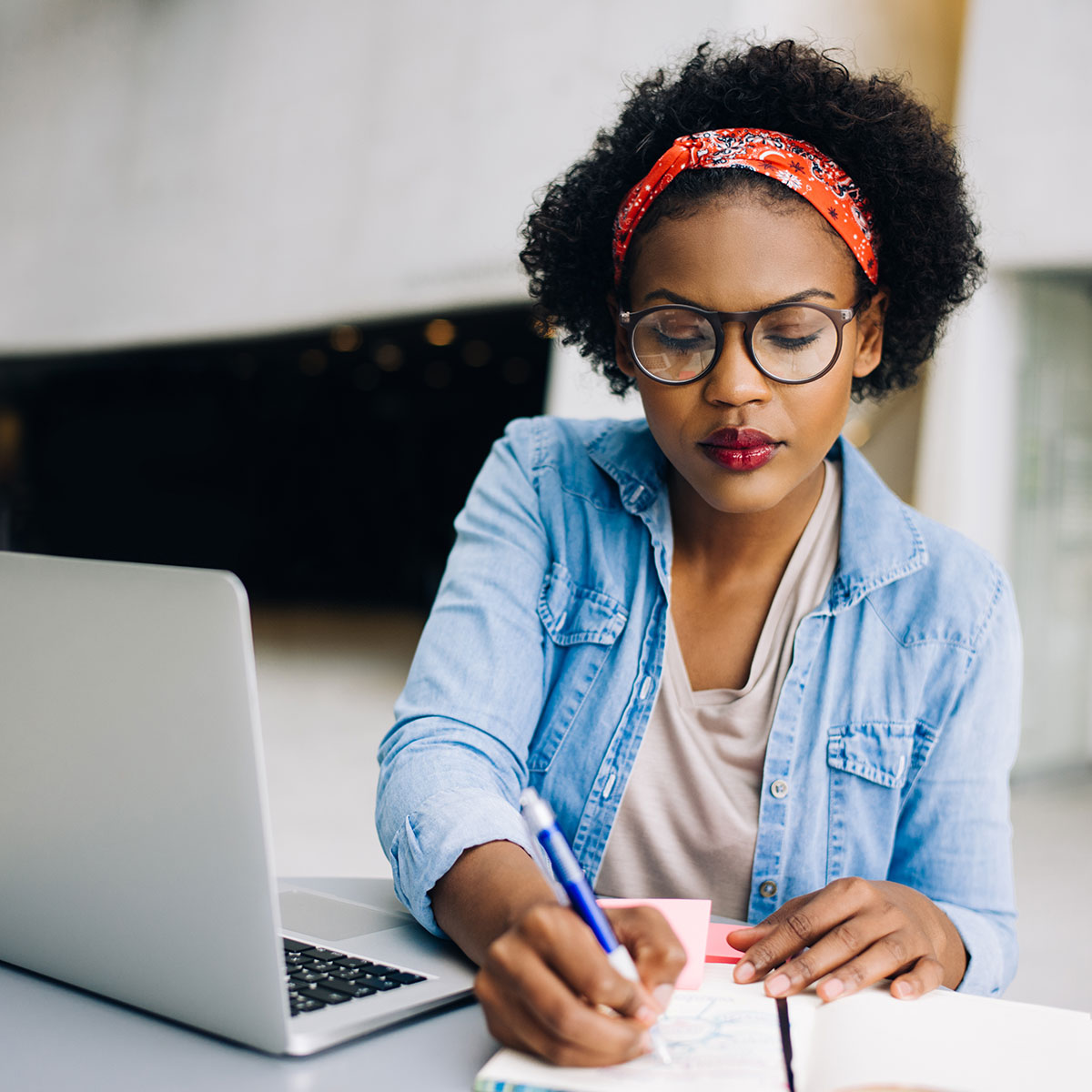 A woman sits at a desk in front of a computer while writing on a piece of paper.