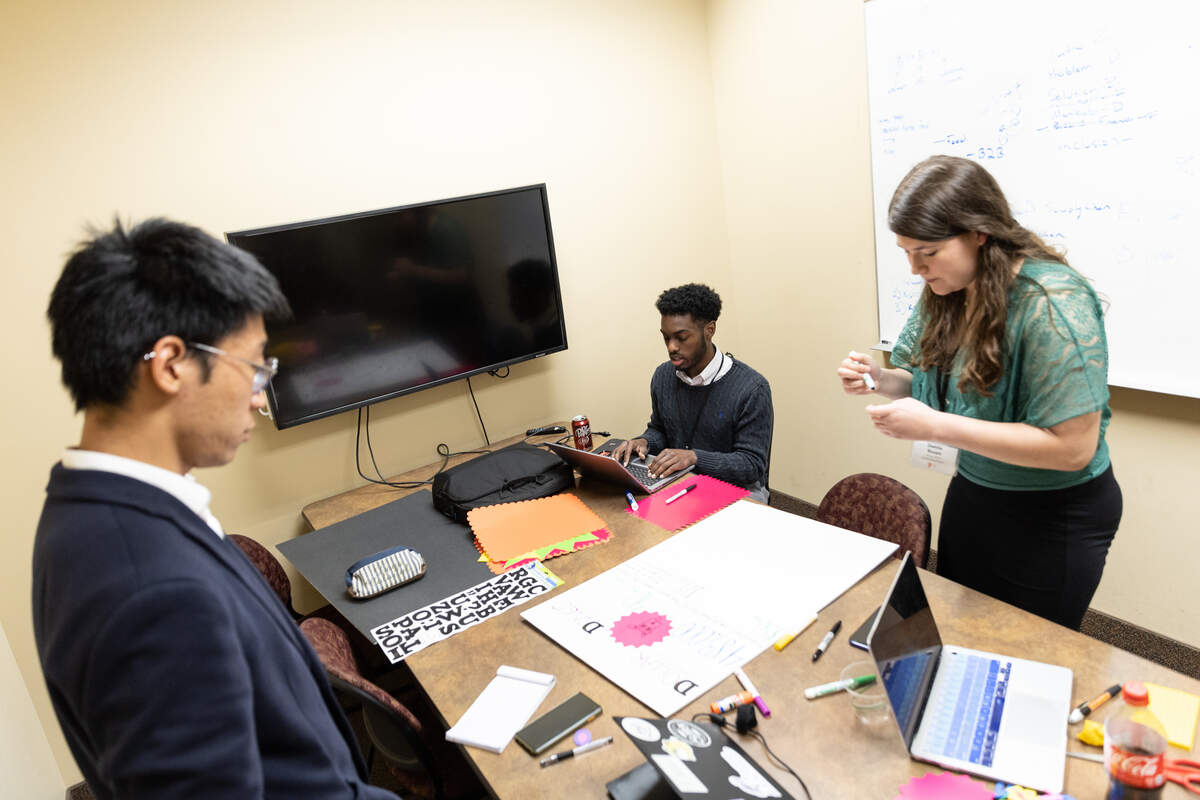 Students at table creating project while one student stands and talks on the phone at eFest.
