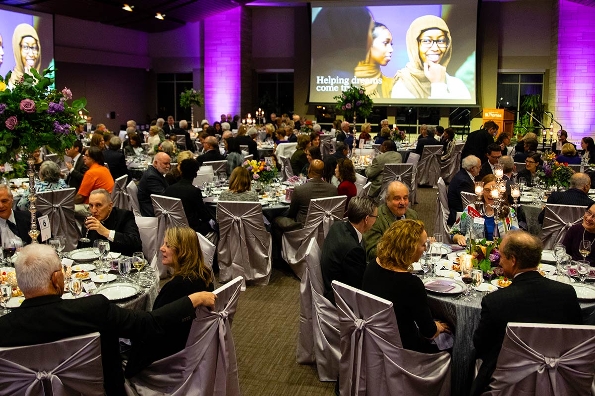 Guests socialize at tables in an event over dinner.