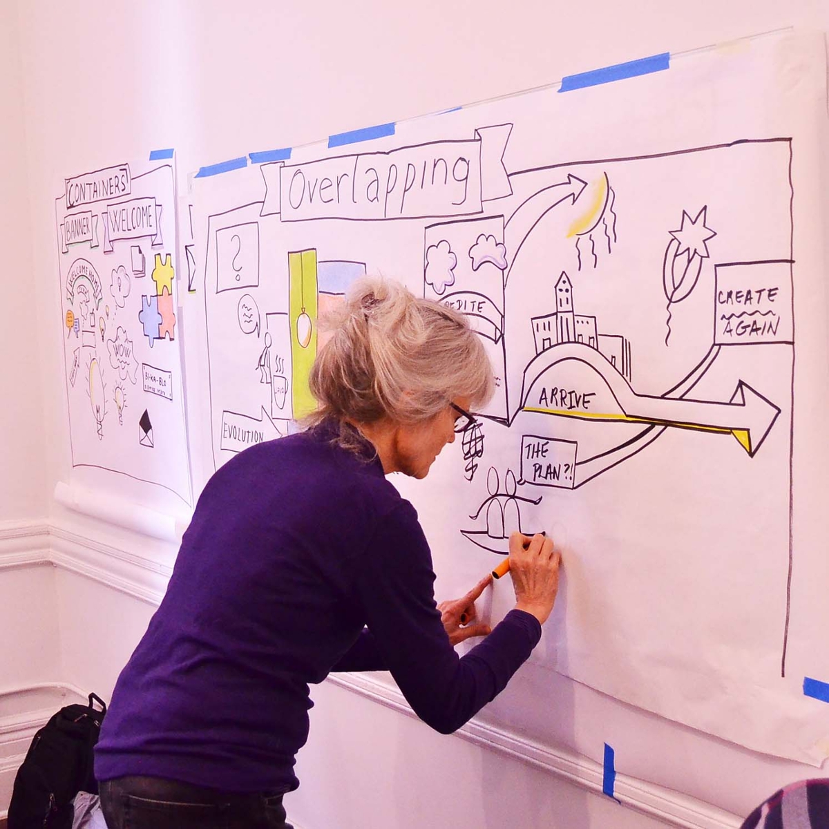 A woman illustrates a project by drawing on large white pieces of paper.