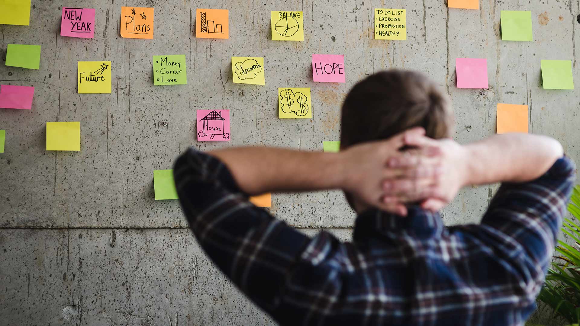 Man looking at a wall covered in post-it notes. 